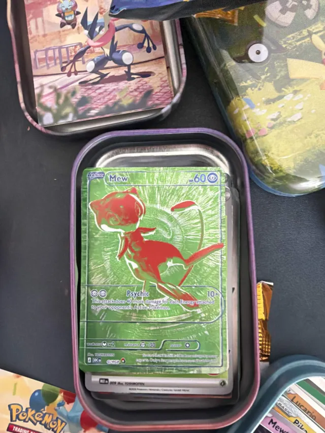 A Mew card pulled from a Pokémon mini tin, the open tin among others